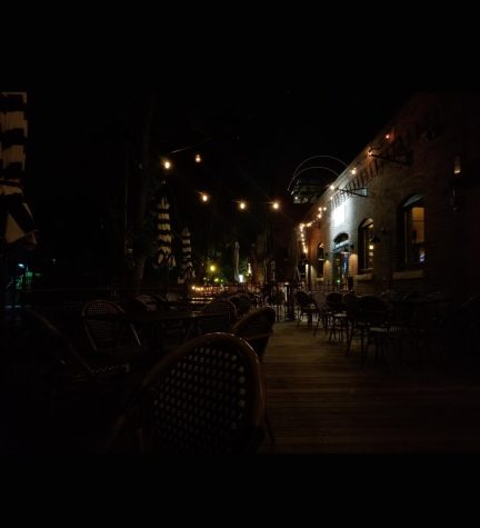A small restaurant patio. Little twinkling lights above vaguely recognizable tables and chairs in the dark summer night